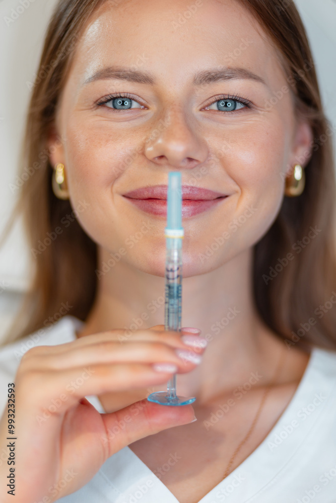 Happy beautiful fresh doctor cosmetologist woman with a smile holds a filler injection near her lips in a medical clinic
