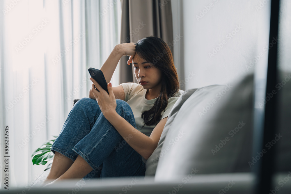 Fototapeta premium Unhappy lonely depressed woman is sitting on the couch and using a phone.