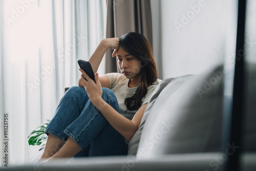 Unhappy lonely depressed woman is sitting on the couch and using a phone.
