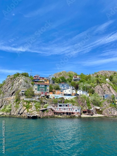 Colourful houses on cliff face near coast with blue sky.