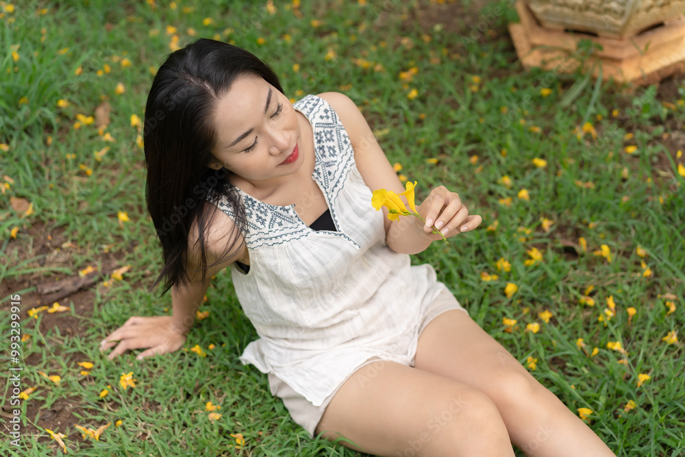 Top view of beautiful smiling woman looking at flowers in hand with tenderness on the grass in a park surrounded by yellow flowers, feeling carefree, enjoying a real happy moment. Lifestyle concept. Top view of beautiful smiling woman looking at flowers in hand with tenderness on the grass in a park surrounded by yellow flowers, feeling carefree, enjoying a real happy moment. Lifestyle concept.