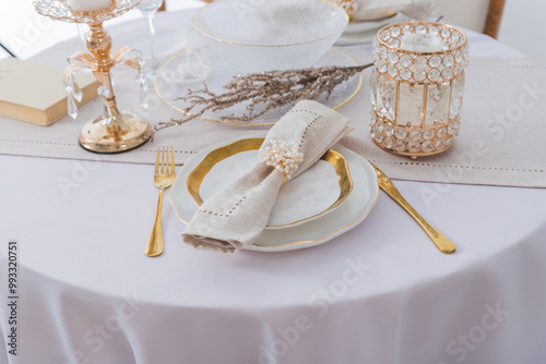 Christmas festive table setting with white plates and gold cutlery, white linen napkin, gifts in white and gold paper, wooden snowflake decoration, paper decorations and balls. Flatlay, blue and gold