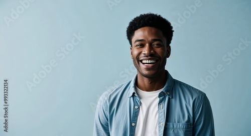 Joyful young African American man with short hair wearing casual shirt on plain light blue background