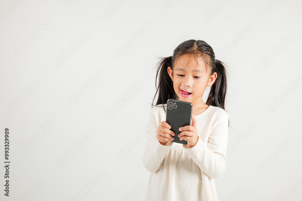 Happy Asian portrait cute young kid girl smiling excited using smart mobile phone studio isolated on white background, Thai kindergarten child surprised holding reading message gesture on smartphone Happy Asian portrait cute young kid girl smiling excited using smart mobile phone studio isolated on white background, Thai kindergarten child surprised holding reading message gesture on smartphone