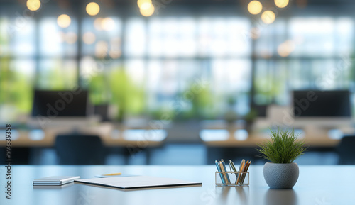 A light-colored desk, with a tablet, pens, and small plant in the foreground. Blurred office space in the background