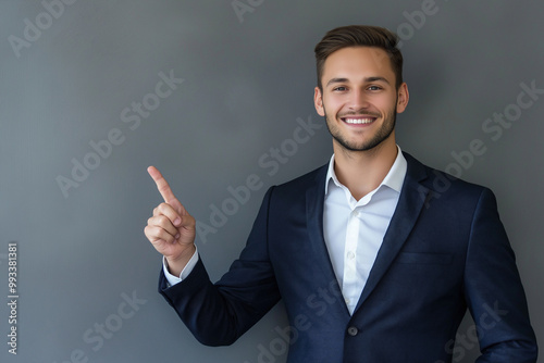 A man in a dark suit and white shirt is smiling and pointing to the right