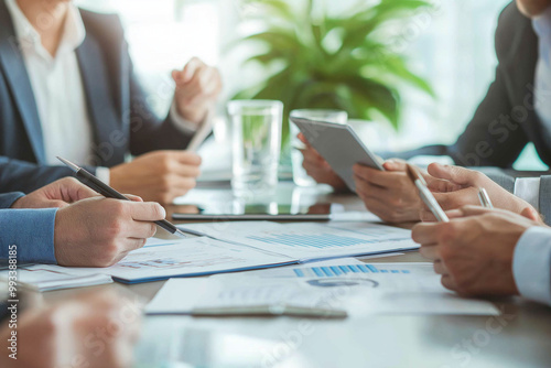 Business people in a meeting, gathered around a table with papers, pens, and tablets