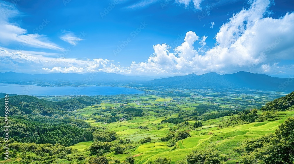 Obraz premium A panoramic view of Kurumayama Plateau with lush green fields, Lake Shirakaba glimmering in the distance, and soft clouds drifting across a blue sky.
