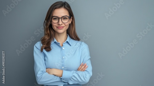Portrait of a confident young woman with glasses wearing a blue shirt on a grey background.