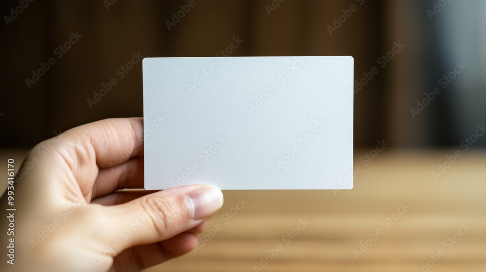 A hand holding a white card against a warm wooden background, evoking a minimalist and elegant feel A hand holding a white card against a warm wooden background, evoking a minimalist and elegant feel