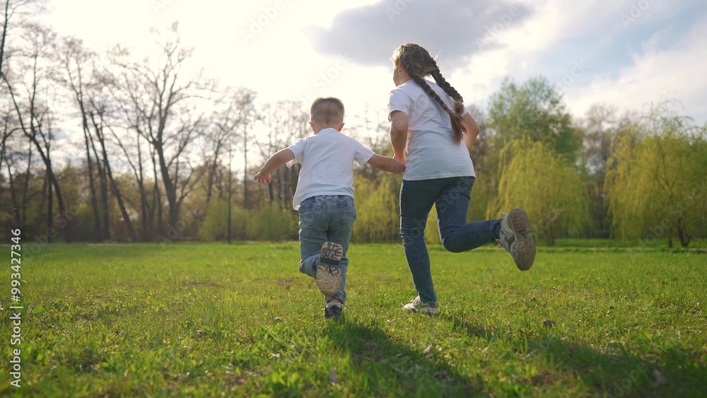 children running across the field. happy family child dream concept. a boy and a girl are running across a green field against the backdrop of a spring forest. child's lifestyle sporty children running across the field. happy family child dream concept. a boy and a girl are running across a green field against the backdrop of a spring forest. child's lifestyle sporty