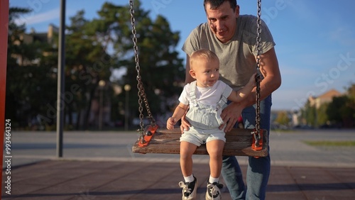 a happy family. dad pushes baby on swing. city . happy child swinging on a swing. fun time. child rides form content lifestyle photo