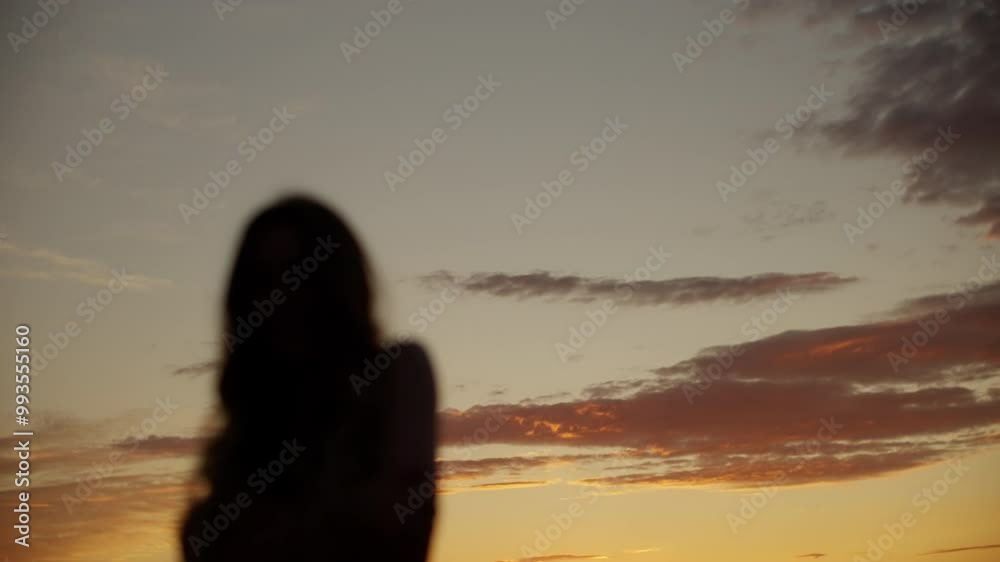 Woman stands gracefully against a backdrop of a setting sun, slightly out of focus and moving slowly. The warm hues of orange, pink, and purple create a serene atmosphere Woman stands gracefully against a backdrop of a setting sun, slightly out of focus and moving slowly. The warm hues of orange, pink, and purple create a serene atmosphere