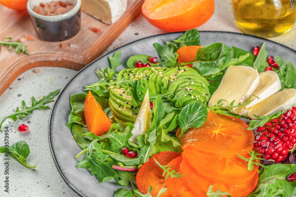 vitamin winter salad with persimmons, fresh greens, avocado, Camembert cheese and pomegranate. organic healthy products. top view vitamin winter salad with persimmons, fresh greens, avocado, Camembert cheese and pomegranate. organic healthy products. top view