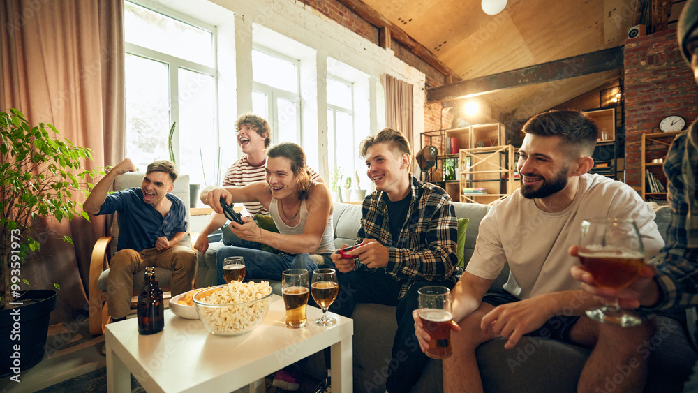 Beers, popcorn, and controllers. Friendly crew completely absorbed in action, with smiles and cheers filling cozy living room. Concept of football fans, sport evens, video games and cybersport. Beers, popcorn, and controllers. Friendly crew completely absorbed in action, with smiles and cheers filling cozy living room. Concept of football fans, sport evens, video games and cybersport.