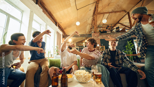 Crucial moment on screen leaves everyone at edge of their seats. Some players pumped, while others facepalm in defeat. Concept of football fans, sport evens, video games and cybersport.