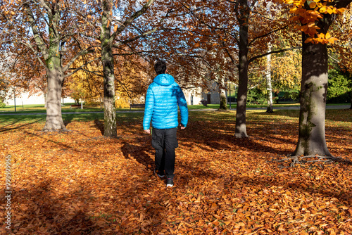 Man with his back to a man in a blue jacket walking through a forest full of trees and orange leaves on the ground typical of autumn on a cold sunny day. photo