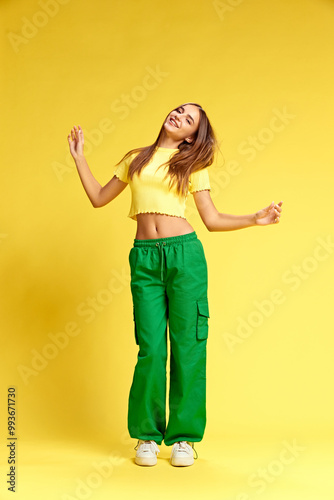 Full-length photo of attractive young, slim woman dressed vibrant clothes dancing of joy against yellow studio background. Concept of human emotions, business, beauty and fashion, sales season. Ad