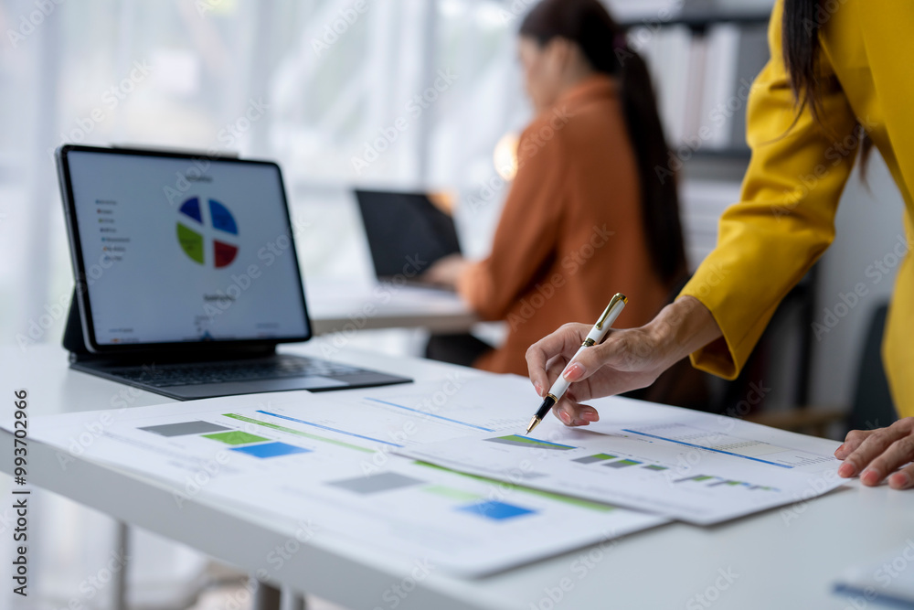 Businesswoman analyzing financial chart using pen pointing on business data chart with partner working in office Businesswoman analyzing financial chart using pen pointing on business data chart with partner working in office