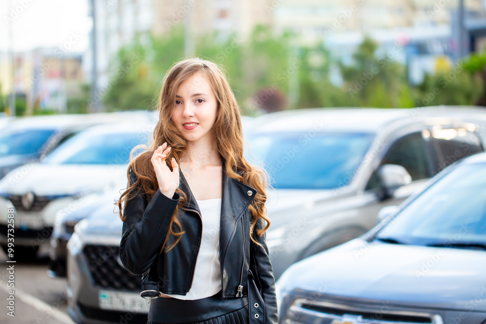 Fototapeta premium A young smiling girl in a good mood walks around the city. Teenage girl, portrait against the background of houses and roads. Fashionable youth style trend.