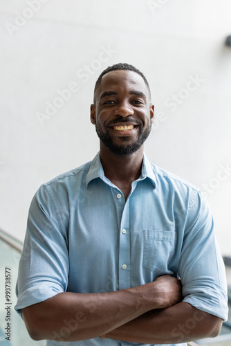 Smiling african american man in blue shirt crossing arms, posing confidently in office setting