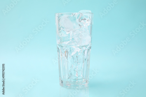 Refreshing water with ice cubes in glass on light blue background