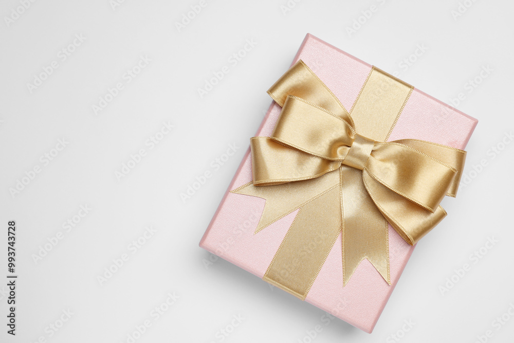 Gift box with golden bow on light grey background, top view. Space for text Gift box with golden bow on light grey background, top view. Space for text