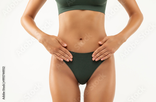 Slim skinny woman in green underwear holding hands, gesturing pain in intimate zone, white background. Maternity fertilization disease infertility concept