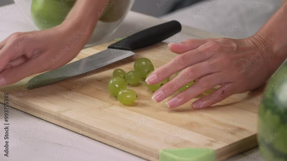 Hands of young woman european puts green grapes on cutting board to prepare fruit salad, right side view close up. Healthy lifestyle concept, raw food diet, cooking at home, refreshing Hands of young woman european puts green grapes on cutting board to prepare fruit salad, right side view close up. Healthy lifestyle concept, raw food diet, cooking at home, refreshing