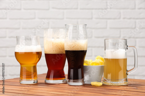 Glasses with different types of beer and snacks on wooden table against white brick wall