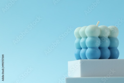 Beautiful bubble candle and podium on light blue background, closeup. Space for text