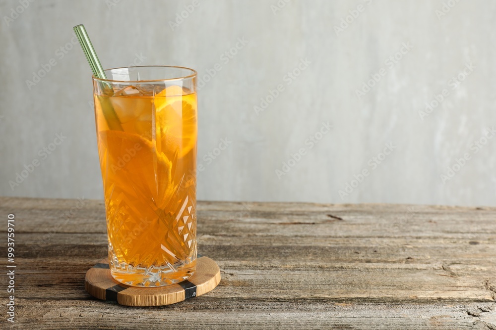 Glass of tasty refreshing drink and straw on wooden table against gray background, space for text