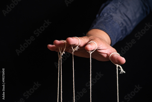 Close-up Of Man Controls The Puppet With Fingers. Man`s Hand Controls The Puppet With The Fingers Attached To Threads Against Black Background,Manipulation concept