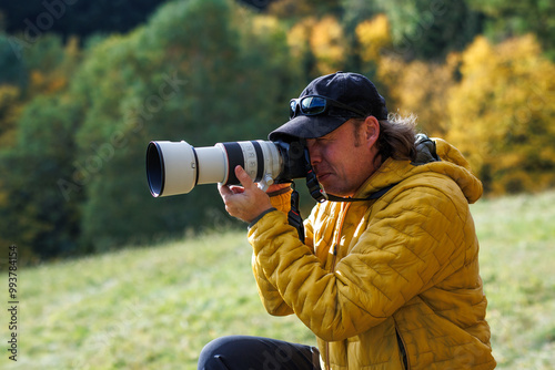 Photographer with camera photographing nature and wildlife in autumn forest
