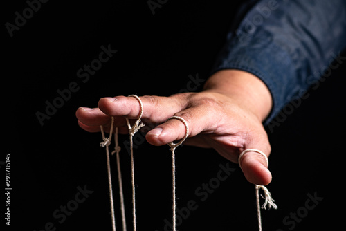 Close-up Of Man Controls The Puppet With Fingers. Man`s Hand Controls The Puppet With The Fingers Attached To Threads Against Black Background,Manipulation concept photo