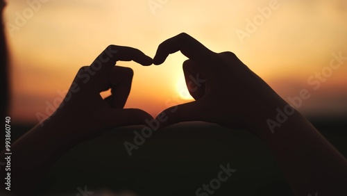 hands make a heart at sunset.happy family kid dream concept. hands in the foreground fold the figure from the fingers. a heart of fingers folded in lifestyle a field at sunset