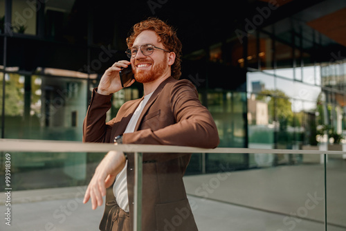 A fashionable businessman is engrossed in a phone call outside a sleek and modern contemporary building