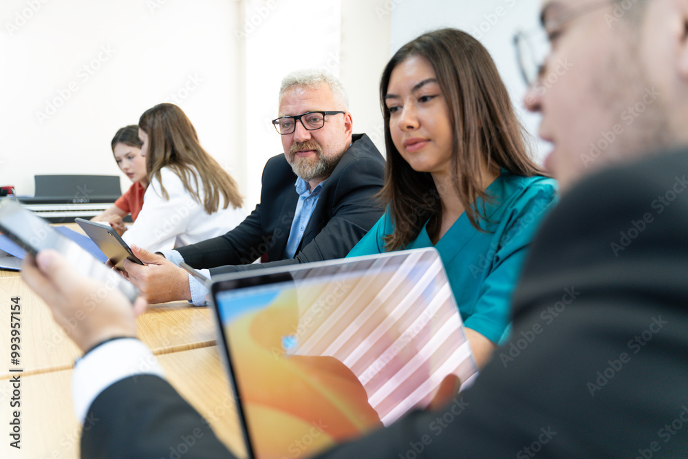 A group of people are sitting at a table with laptops and a projector. They are likely discussing a project or presentation