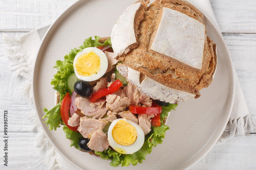 Tuna nicoise sandwich also known as pan bagnat closeup on the plate on the wooden table. Horizontal top view from above