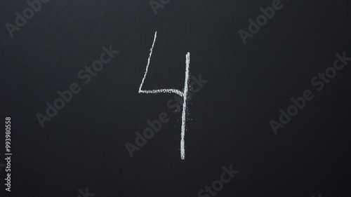 Hand writes the number 4 with white chalk on a black board
