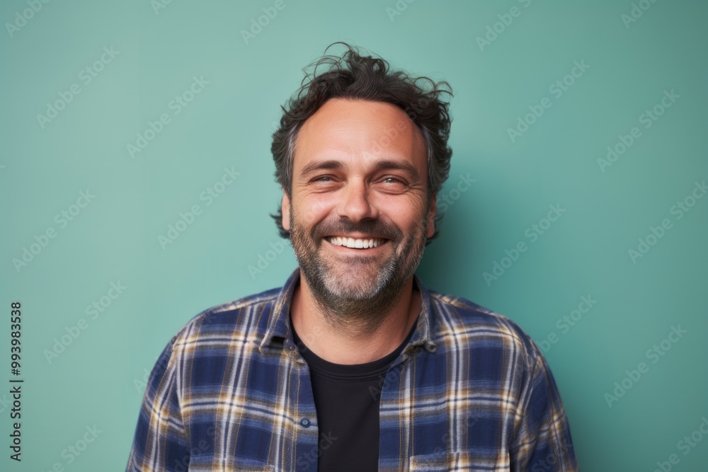 Portrait of a grinning man in his 40s wearing a comfy flannel shirt in solid pastel color wall Portrait of a grinning man in his 40s wearing a comfy flannel shirt in solid pastel color wall