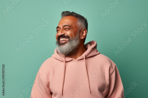 Portrait of a joyful indian man in his 50s sporting a comfortable hoodie over solid pastel color wall