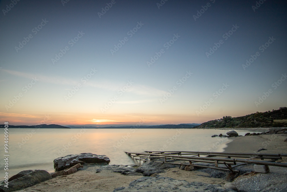 View through rocks on a sandy beach into the sunset. Landscape shot with a view to the horizon over the wide sea on the coast of Ouranoupoli, Thessaloniki, Central Macedonia, Greece View through rocks on a sandy beach into the sunset. Landscape shot with a view to the horizon over the wide sea on the coast of Ouranoupoli, Thessaloniki, Central Macedonia, Greece