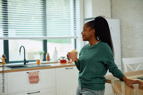 Happy black woman enjoying in cup of tea in kitchen.