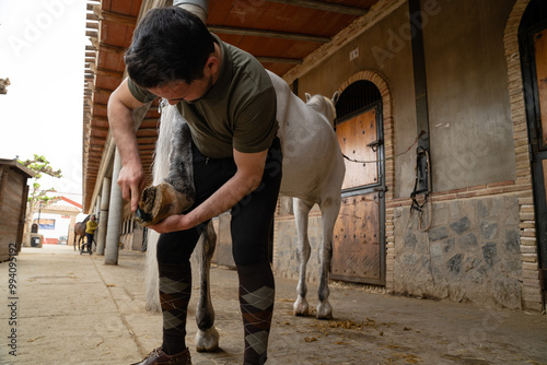 Man cleaning his horse's shoes in a stable with a brush and a clinch cutter . copy space right