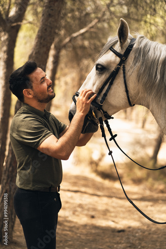 Young boy looking lovingly at his white horse. They are in a forest. Vertical photo.