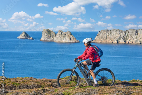 active senior woman cycling with her electric mountain bike along the wild coast of Finisterre in southern Brittany next to Camaret-sur-Mer, France