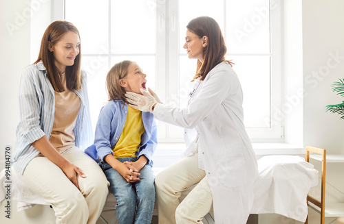 Dentist doctor or nurse conducts an examination on boy patient at the clinic. Boy mother is present during the medical treatment, as the healthcare professional provides dentistry care for the child.