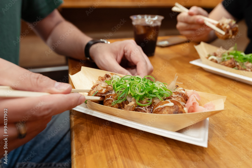 A man is taking a takoyaki ball with his chopsticks in a bar with friends. A popular street food in Osaka, Japan