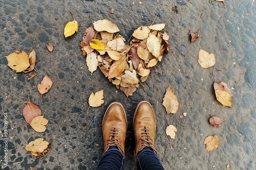 Heart-shaped autumn leaves with brown boots on wet pavement. A Walk Through Golden Leaves photo